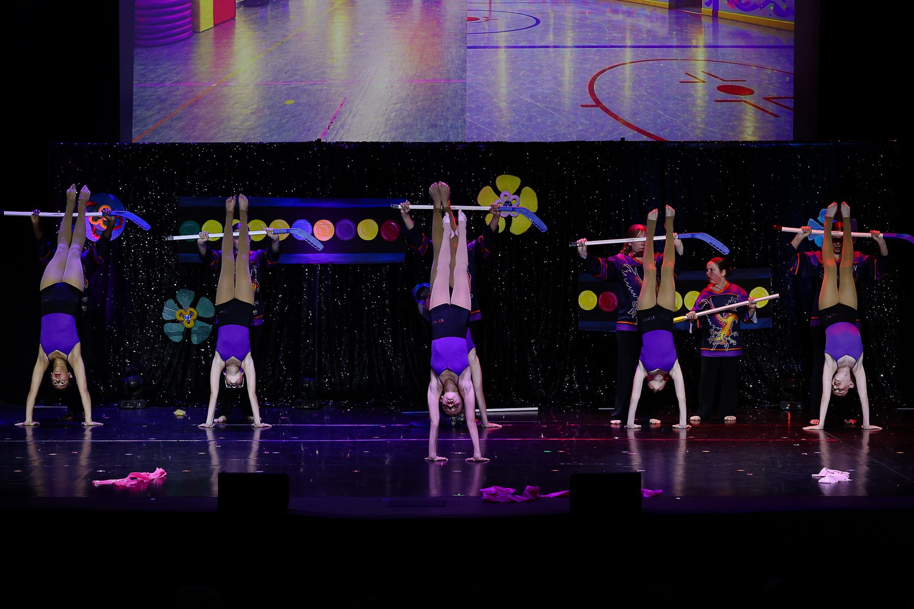 Acro dancers holding handstands beneath hockey sticks at an Ignite Your Flare recital