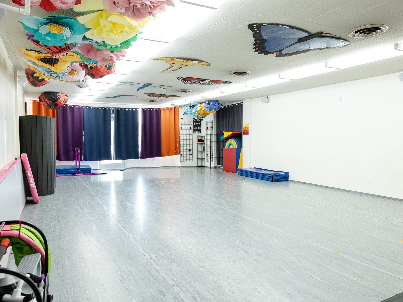 Studio 1 looking toward the front windows, with mats, a kip bar and colorful curtains