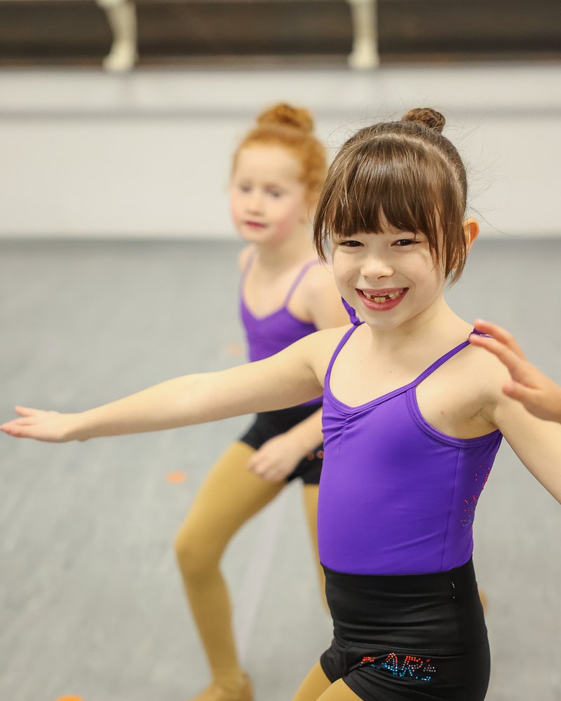 Smiling dancer in the purple leotard, black shorts and tan tights